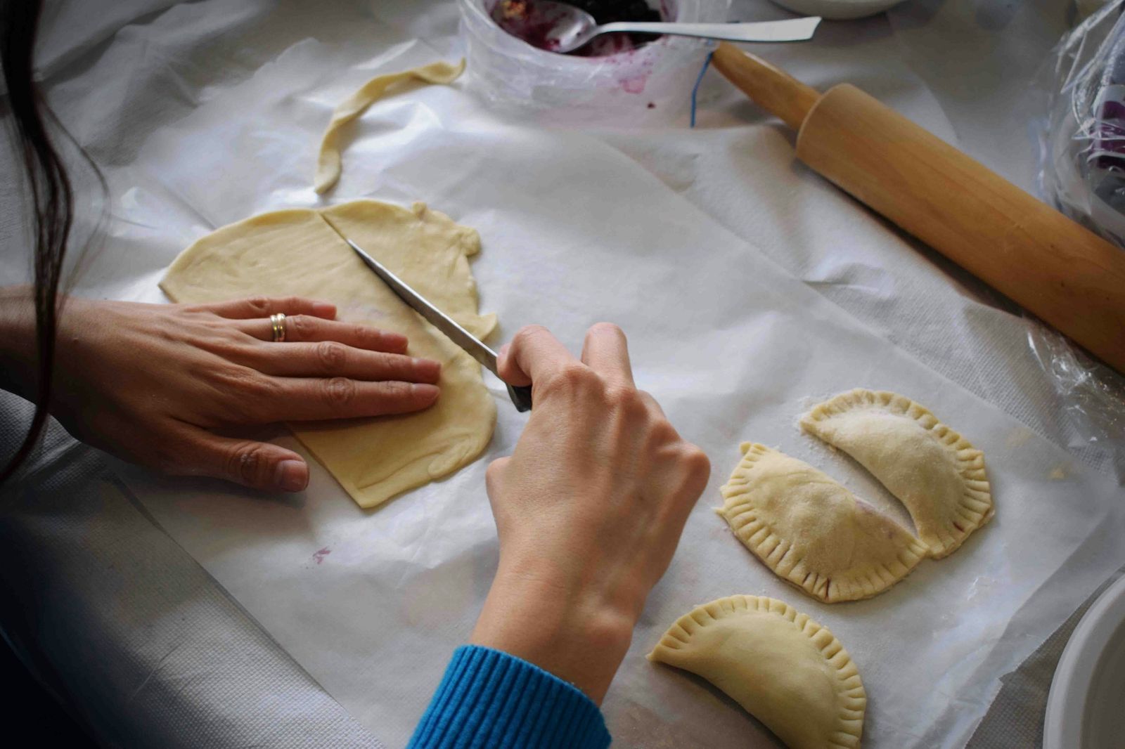 Hands folding empanadas on a floured table
