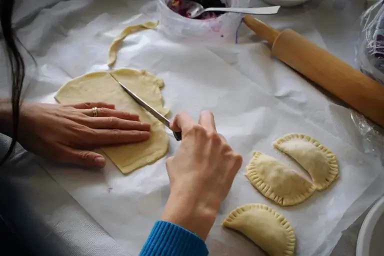 Hands folding empanadas on a floured table