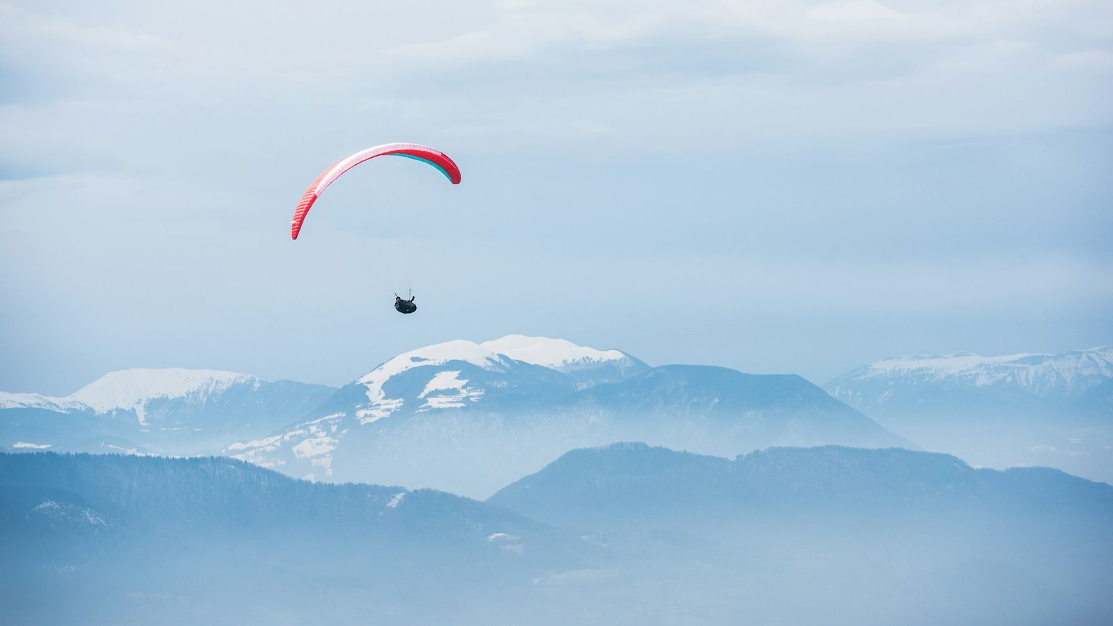 A paraglider flying above mountain ridges
